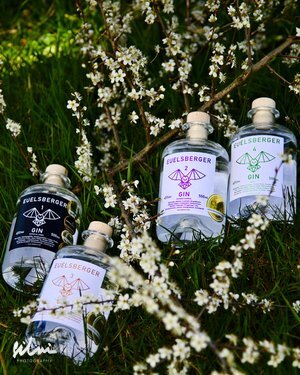 Four Fuelsberger Gin bottles with distinct labels on grass amid white blossom branches