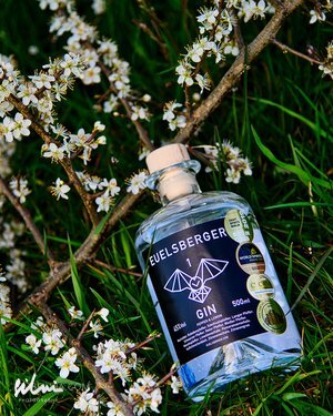 Neuelsberger Gin bottle with bat logo and awards on grass beside white flowering branch