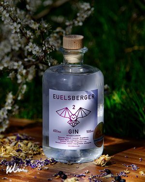 Clear Euelsberger Gin bottle with wooden cap on wood surrounded by dried petals and flowers.