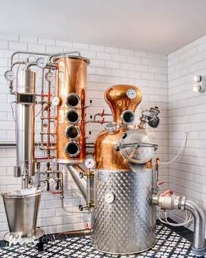 Copper and stainless steel distillation apparatus with gauges and valves in tiled room.