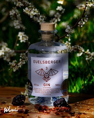 Bottle of Euelsberger Gin 45% 500ml with cork stopper on wooden surface with blossoms and botanicals.