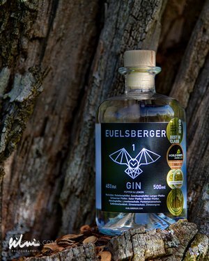 Bottle of Euelsberger Gin 500ml with black label and award emblems against tree bark.