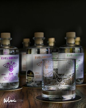 Clear glass with geometric bat design in front of EUELSBERGER gin bottles on wooden surface