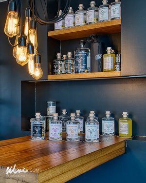 Wooden shelves and countertop with assorted gin bottles under hanging Edison light bulbs.