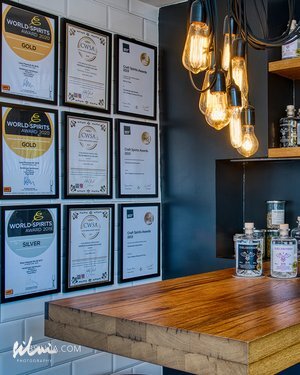 Wooden countertop with hanging Edison bulbs and a wall of framed awards in a bar interior.
