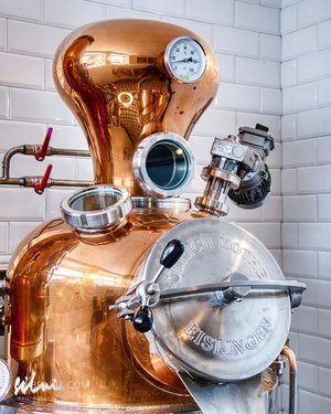 Copper distillation apparatus with pressure gauge, valves, and embossed circular metal door.