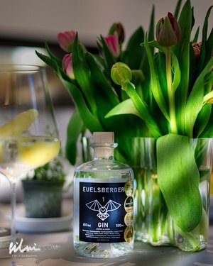 Bottle of Euelsberger Gin next to a wine glass with lemon and pink tulips in a vase