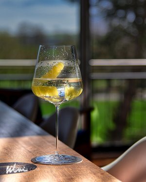 Wine glass with sparkling clear drink and lemon peel on wooden table near a window.