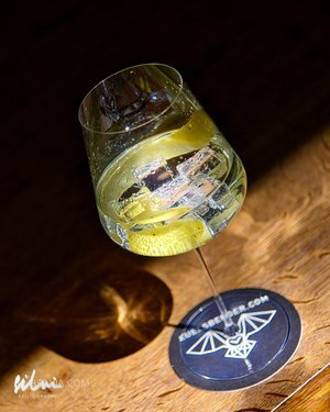 Glass with clear beverage and ice on a dark coaster with bat design on wooden surface.
