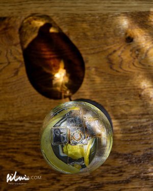 Top-down view of a glass with ice cubes and a lemon slice on a wooden surface with shadows.