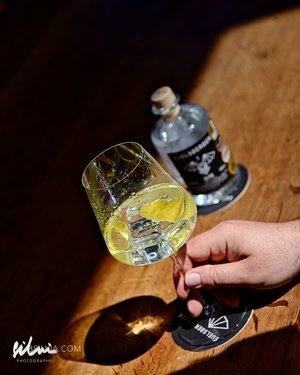Hand holding a wine glass with yellow drink and ice, bottle on wooden surface nearby.