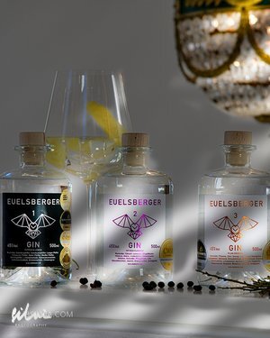 Three EUELSBERGER gin bottles numbered 1, 2, 3 with labels, juniper berries, lemon twist, and chandelier.