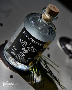 Bottle of Euelsberger Gin with cork stopper, black label, herbs, and peppercorns nearby.