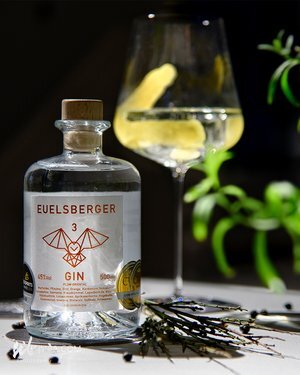 Bottle of Euelsberger Gin with herbs on a surface and a glass with garnish in the background