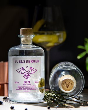 Bottle of EUELSBERGER Gin with a purple label and wooden cap, accompanied by a glass with lemon garnish.