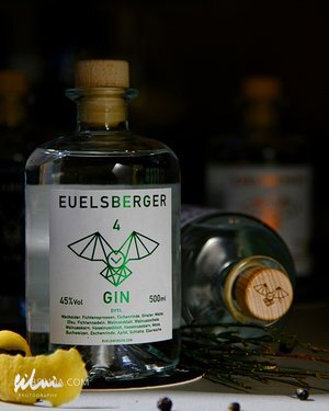 Clear bottle of EUELSBERGER 4 Gin with wooden cap, 45% alcohol, 500ml, herbs and lemon nearby.