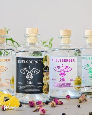 Four EUELSBERGER gin bottles with different colored labels and wooden caps on a white surface.