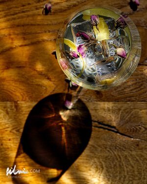 Glass with ice, lemon slices, and dried flowers on wooden surface with shadow.