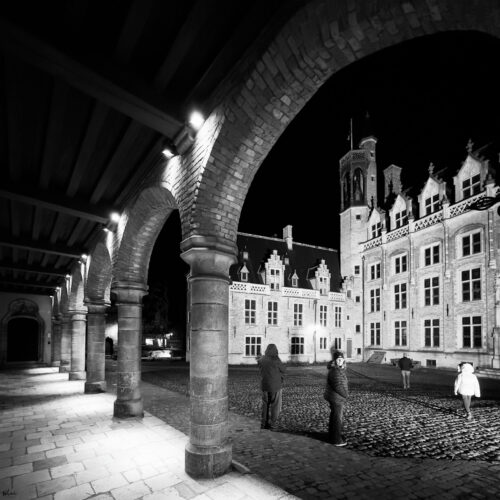 Historic courtyard at night with stone arches, cobblestone pavement, and lit ornate buildings.